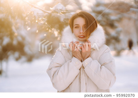 Beautiful woman in winter clothes posing in a snowy park. Young lady walking in a sunny winter day. Beautiful woman in winter clothes posing in a snowy park. Young lady walking in a sunny winter day. 95992070