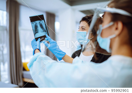 A female doctor in visor and protective gloves discussing an x-ray. Doctor examines an X-ray. A female doctor in visor and protective gloves discussing an x-ray. Doctor examines an X-ray. 95992901