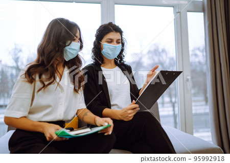 Two business colleagues in protective face mask discussing work related matters on an office. 95992918