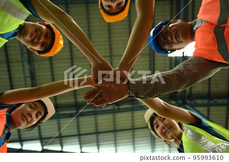 Smiling warehouse workers team stacking hands together bottom view. Unity, supporting and teamwork concept 95993610