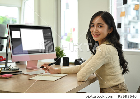 Confident female photo editors sitting in creative workplace front of personnel computer and smiling to camera 95993646