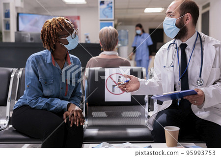 Healthcare professional receiving african american patient in hospital room. Doctor attending sick woman in clinic waiting area. Medical staff, people wearing masks at sanatorium reception. 95993753