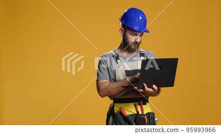 Portrait of handyman using laptop to find construction inspiration and work on refurbishment scheme or plan. Browsing internet on pc to do measurement and engineering process in studio. 95993966