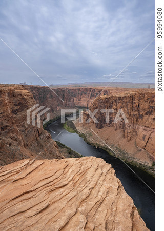 Aerial View Of Colorado River Flowing Amidst Majestic Canyons Against Cloudy Sky At Glen Canyon Dam In Arizona 95994080