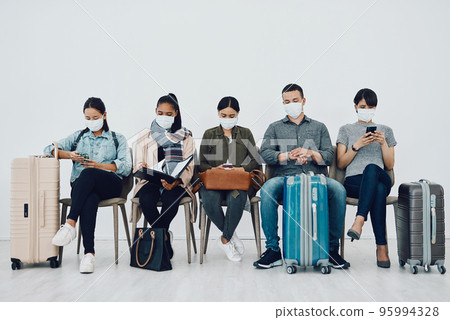Covid-19 came to our country. Shot of a group of young people wearing masks while waiting together in an airport lounge. 95994328