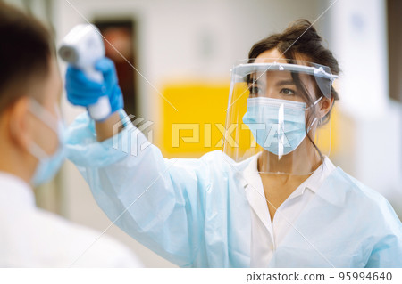 Temperature screening office workers. Disease control expert in visor with an Infrared thermometer. Temperature screening office workers. Disease control expert in visor with an Infrared thermometer. 95994640