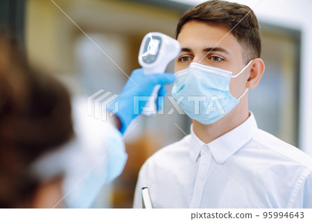 Temperature screening office workers. Disease control expert in visor with an Infrared thermometer. Temperature screening office workers. Disease control expert in visor with an Infrared thermometer. 95994643