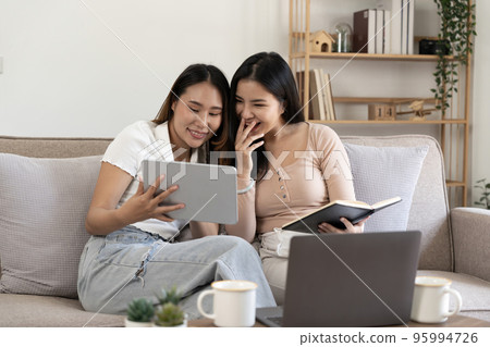 Happy two young asian girls are sitting on couch using digital tablet at home Happy two young asian girls are sitting on couch using digital tablet at home 95994726