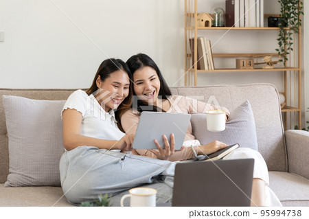 Happy two young asian girls are sitting on couch using digital tablet at home 95994738