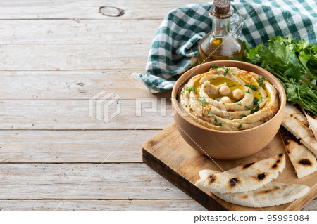 Chickpea hummus in a wooden bowl garnished with parsley, paprika and olive oil on wooden table 95995084