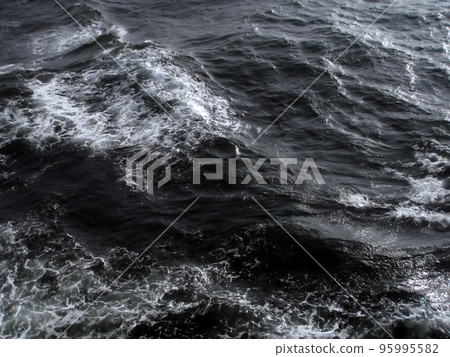 On a stormy night, a dark scene of waves spraying from the rough sea. 95995582