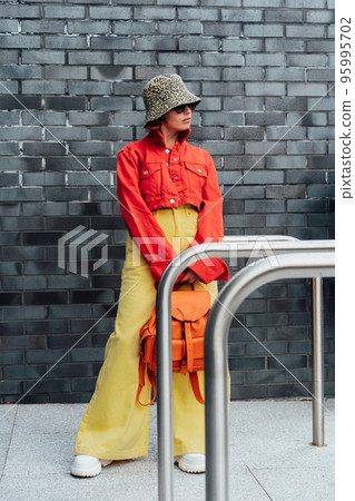 Hipster fashion young woman in bright clothes, sun glasses and bucket hat on the gray brick wall background. Urban city street fashion. Vertical card. Selective focus. Copy space 95995702