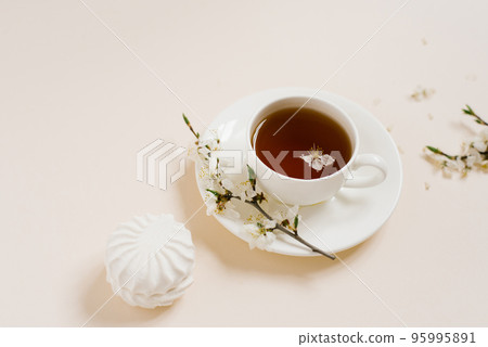 Tea cup standing with apple flowers and marshmallow on beige background Tea cup standing with apple flowers and marshmallow on beige background 95995891