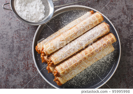 Homemade wafer rolls with condensed milk, a favorite treat of childhood closeup in plate. Horizontal top view Homemade wafer rolls with condensed milk, a favorite treat of childhood closeup in plate. Horizontal top view 95995998