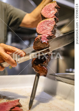 Picanha is a BBQ Steak meat grilled in charcoal. Knife cutting on skewer. Brazilian meat in a Churrascaria restaurant 95996314