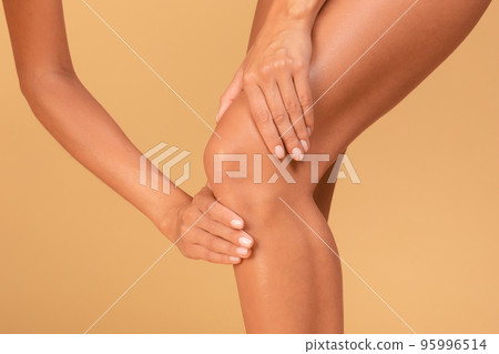 Legs problems. Young caucasian woman touching her inflamed knee with acute pain, beige background, closeup, cropped Legs problems. Young caucasian woman touching her inflamed knee with acute pain, beige background, closeup, cropped 95996514