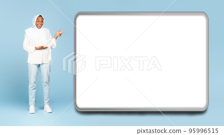 Wow, look here. Happy black muslim woman pointing at big blank device display, showing huge white empty screen Wow, look here. Happy black muslim woman pointing at big blank device display, showing huge white empty screen 95996515