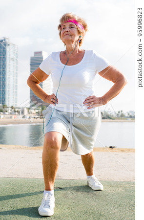 Aged woman doing fitness moves on beach Aged woman doing fitness moves on beach 95996823