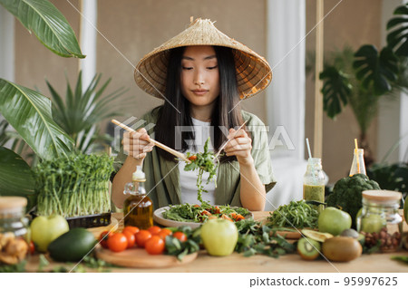 Beautiful asian woman making healthy salad stirring chopped leaves indoor at exotic light studio. 95997625