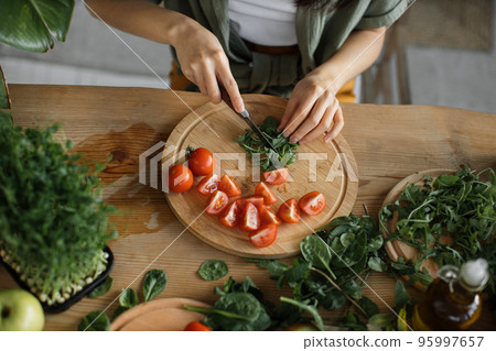 High angle view of hands of woman chopping arugula leaves, sitting at table in bright exotic studio High angle view of hands of woman chopping arugula leaves, sitting at table in bright exotic studio 95997657