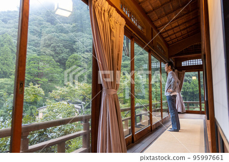 A middle-aged man looking at the outside scenery from the window of the inn where he is staying while traveling A middle-aged man looking at the outside scenery from the window of the inn where he is staying while traveling 95997661