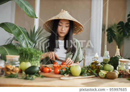 Young asian woman blogger or content creator choping tomatoes preparing vegan salad 95997685