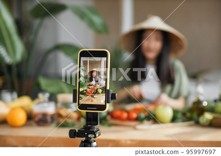 Young asian woman blogger or content creator chopping tomatoes preparing vegan salad Young asian woman blogger or content creator chopping tomatoes preparing vegan salad 95997697