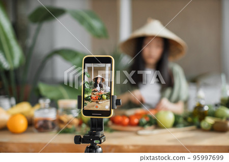 Young asian woman blogger or content creator chopping tomatoes preparing vegan salad Young asian woman blogger or content creator chopping tomatoes preparing vegan salad 95997699