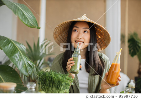 Young and happy asian woman in traditional conical hat drinking healthy tonic smoothie Young and happy asian woman in traditional conical hat drinking healthy tonic smoothie 95997710