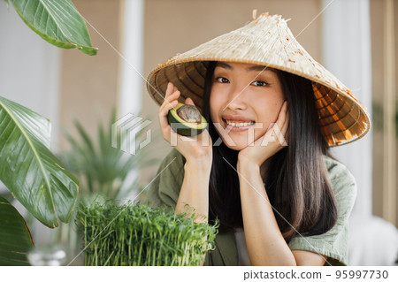 Joyful asian woman in traditional hat making vegetable and fruit salad enjoying healthy dinner Joyful asian woman in traditional hat making vegetable and fruit salad enjoying healthy dinner 95997730