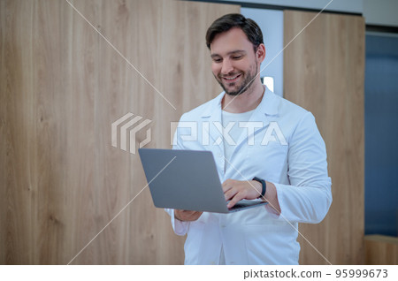 Doctor in a lab coat with a laptop having a session online Doctor in a lab coat with a laptop having a session online 95999673