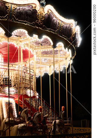 Children's Carousel spinning at an amusement park in the evening at night illumination. Outdoor vintage colorful luminous carousel in the dark. Retro Carousel details, horses. Christmas entertainment Children's Carousel spinning at an amusement park in the evening at night illumination. Outdoor vintage colorful luminous carousel in the dark. Retro Carousel details, horses. Christmas entertainment 96000200