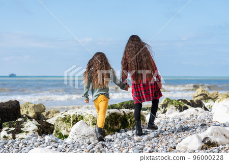 Back view of two little girls in red tartan dress, green jumper and yellow leggings walking at Hope Gap beach near Cuckmere Haven located between Seaford and Eastbourne in East Sussex, UK Back view of two little girls in red tartan dress, green jumper and yellow leggings walking at Hope Gap beach near Cuckmere Haven located between Seaford and Eastbourne in East Sussex, UK 96000228