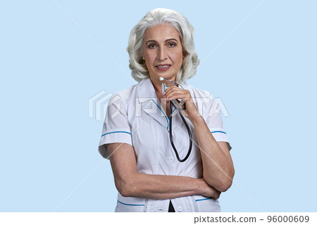 Portrait of aged gray-haired female doctor holding stethoscope. Isolated on pale blue background. 96000609