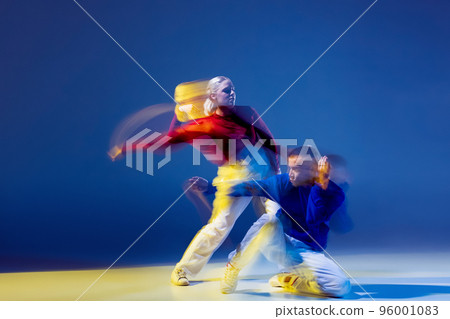Portrait of young man and woman dancing isolated over dark blue background with mixed lights. Breakdance, hip-hop 96001083