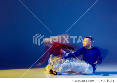 Portrait of young man and woman dancing isolated over dark blue background with mixed lights. Breakdance 96001084