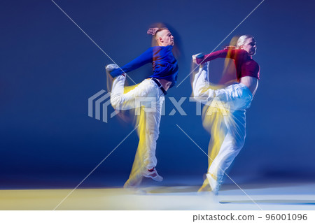 Portrait of young man and woman synchronically dancing isolated over dark blue background with mixed lights 96001096
