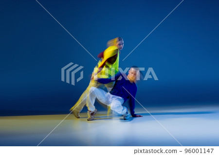 Portrait of young man and woman dancing isolated over dark blue background with mixed lights. Sport achievement, expression. 96001147