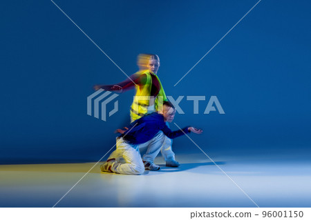 Portrait of young man and woman dancing isolated over dark blue background with mixed lights. Colorful costumes 96001150
