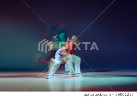 Portrait of young man and woman dancing isolated over dark blue background with mixed lights. Sportive lifestyle 96001255