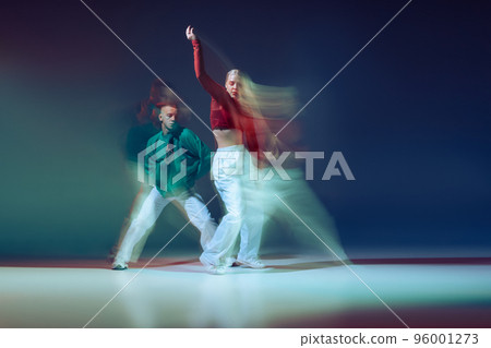 Portrait of young man and woman dancing isolated over dark blue background with mixed lights. Casual look 96001273