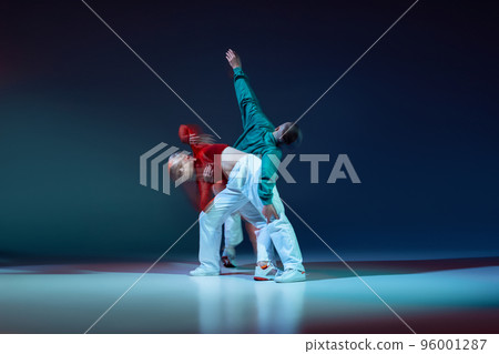 Portrait of young man and woman expressively dancing dancing isolated over dark blue background with mixed lights Portrait of young man and woman expressively dancing dancing isolated over dark blue background with mixed lights 96001287