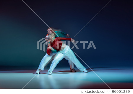Portrait of young man and woman dancing, performing hip-hop, contemp isolated over dark blue background with mixed lights Portrait of young man and woman dancing, performing hip-hop, contemp isolated over dark blue background with mixed lights 96001289