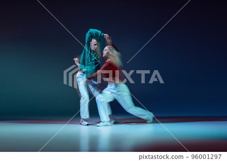 Portrait of young couple, man and woman performing on stage isolated over dark blue background with mixed lights. Hip-hop dance 96001297