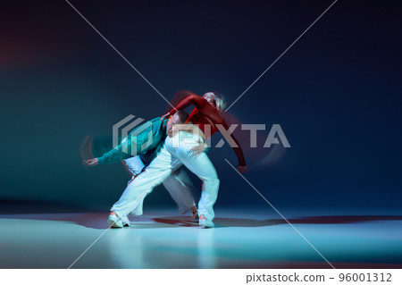 Portrait of young man and woman dancing isolated over dark blue background with mixed lights. Emotional dance 96001312