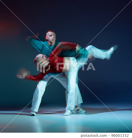 Portrait of young man and woman dancing contemporary dance isolated over dark blue background with mixed lights 96001332