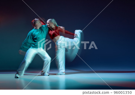 Portrait of young couple, man and woman dancing modern style dance isolated over dark blue background with mixed lights 96001350