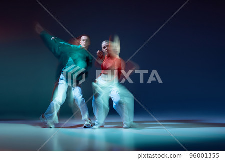 Portrait of young man and woman dancing contemp isolated over dark blue background with mixed lights. Red and green outfits 96001355