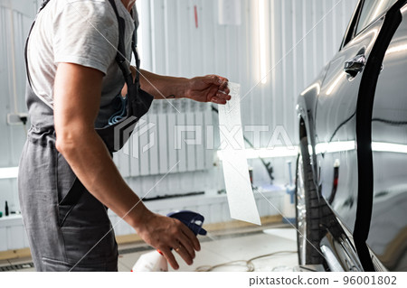 Worker applies car protection film on a car in detailing service Worker applies car protection film on a car in detailing service 96001802
