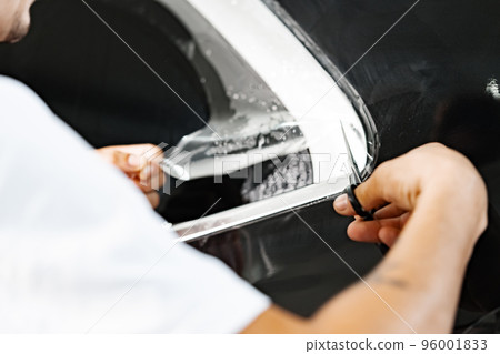 Car wrapping specialist wraps a car with adhesive film in car detailing service Car wrapping specialist wraps a car with adhesive film in car detailing service 96001833